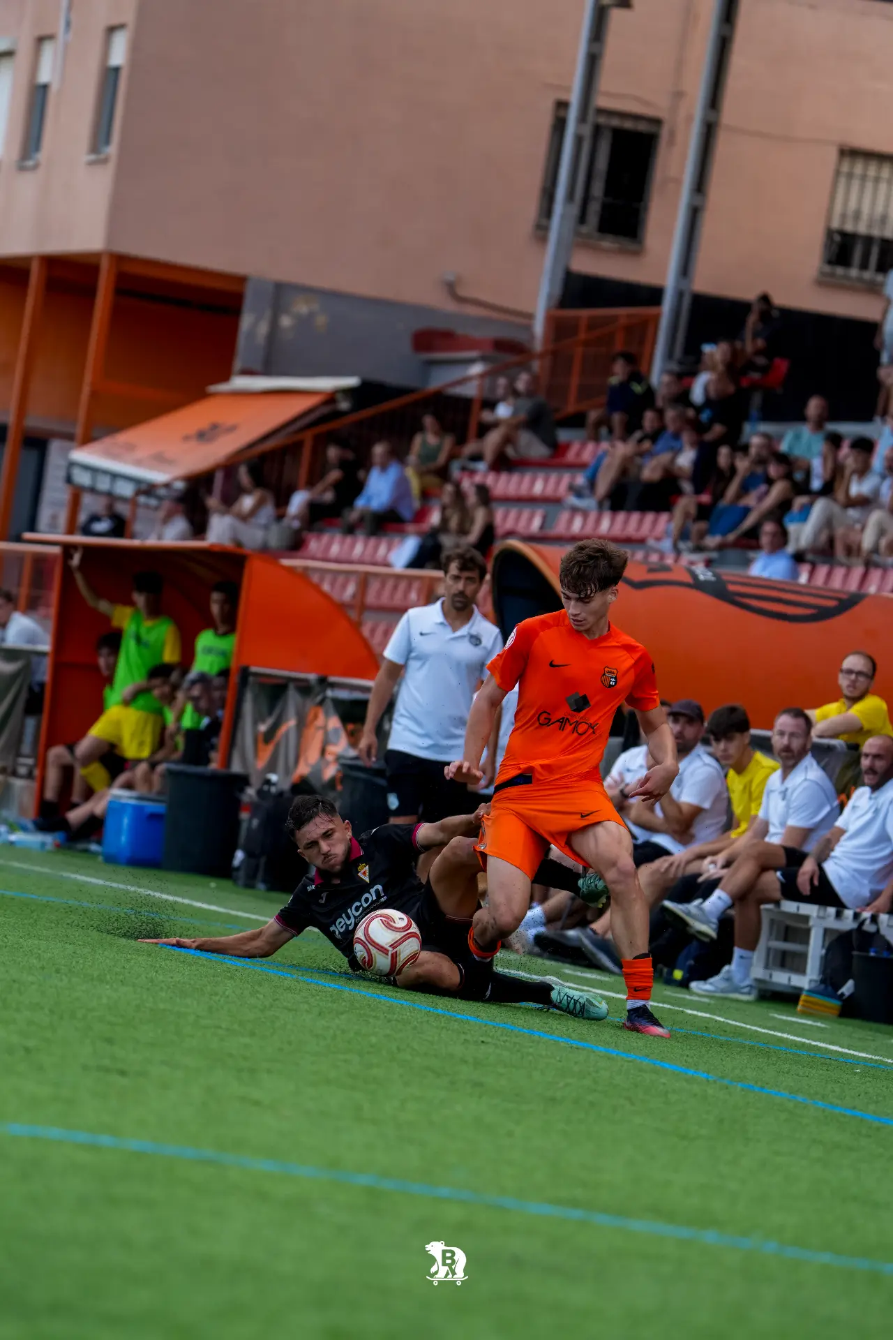 Un jugador del Torrent CF supera la entrada de un rival del Murcia Promises junto al banquillo